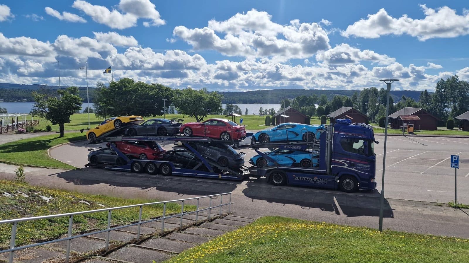 Autotransporter von Spedition HTL mit Sportwagen beladen an einem See — Luxusfahrzeugtransport